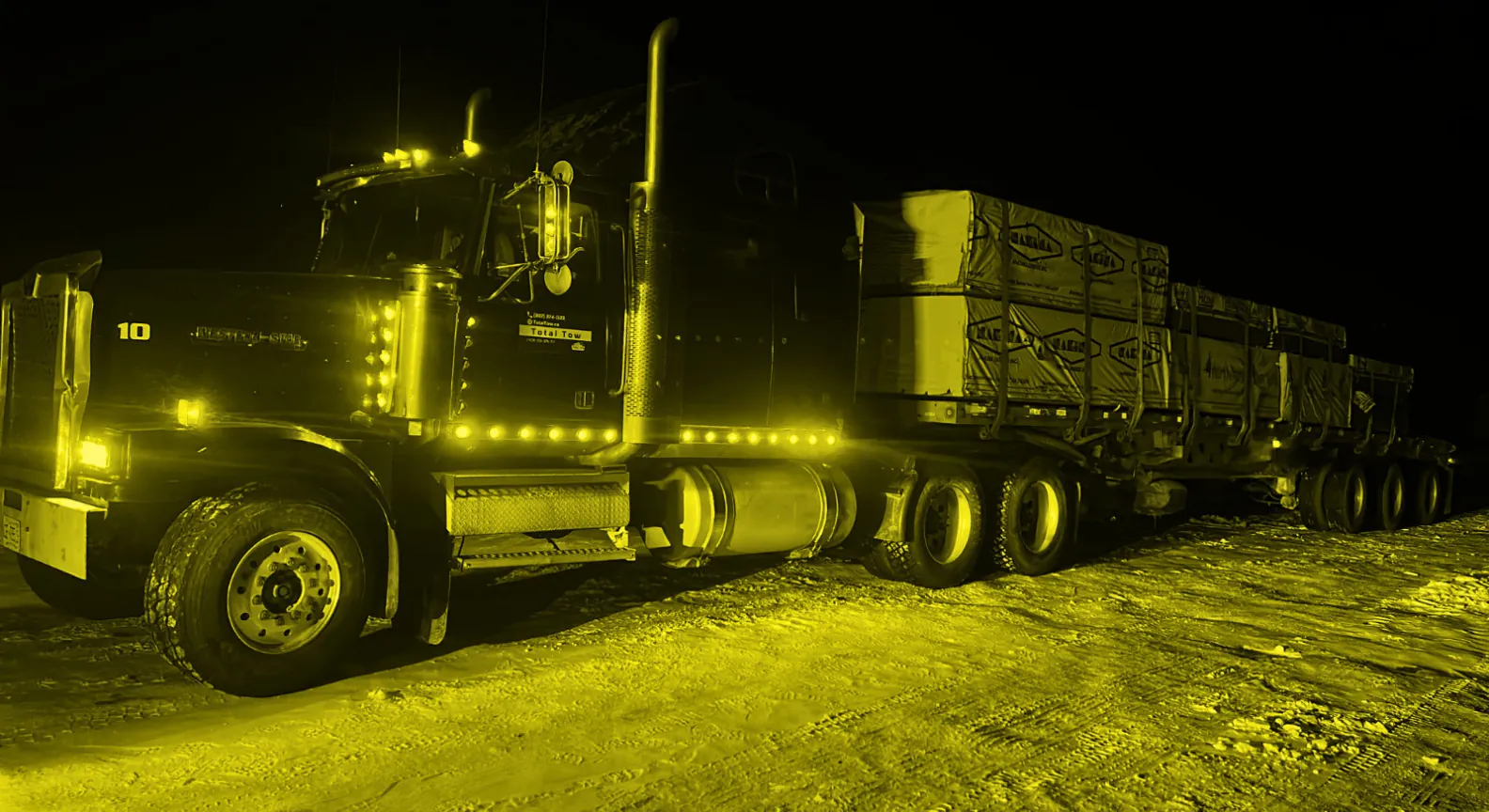 A loaded Total Trucking flatbed pulling out of the yard at night, ready to roll